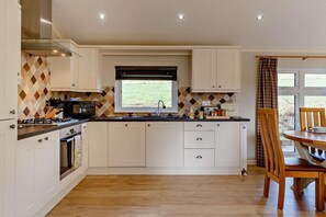 Una cocina moderna con armarios blancos, una isla central, un ventanal con vistas, y un comedor con una mesa y sillas de madera.