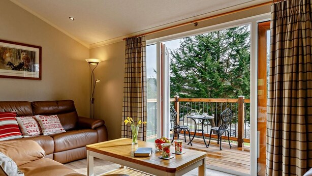 A living room with a sofa, a coffee table, and a view of an outdoor deck with chairs.