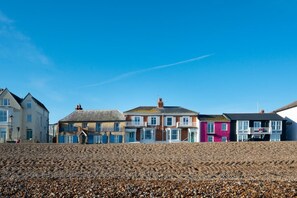 Une rangée de maisons au bord de la mer, avec une plage de galets au premier plan.