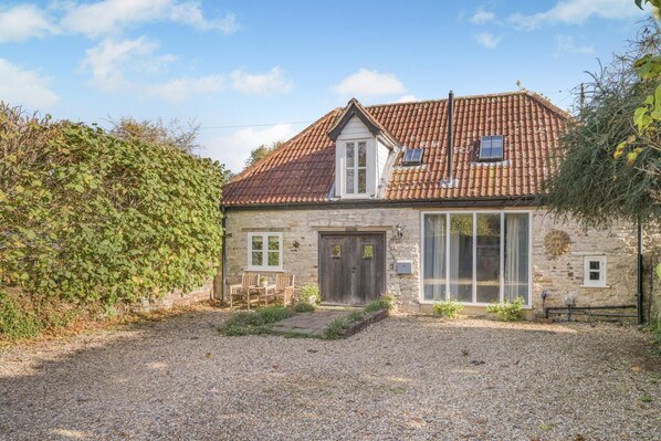 A stone house with a tiled roof, a front door, and a small garden area.