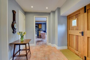 A hallway with a wooden door, a clock, and a table with flowers.