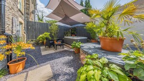Ein Patio mit Gartenmöbeln, einem Whirlpool und verschiedenen Kübelpflanzen.