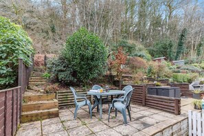 Een terras met een tafel en stoelen, omringd door een houten hek en verschillende planten.