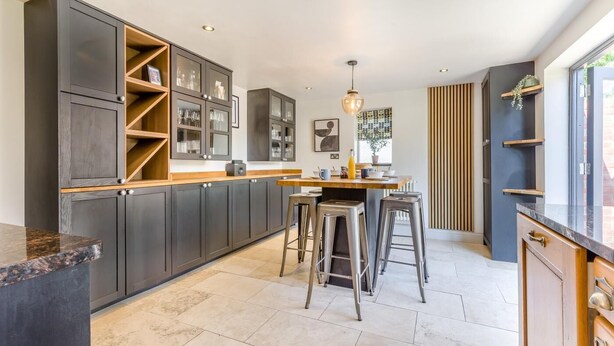 A modern kitchen with dark cabinets, a wooden countertop, and bar stools. - 6 Bed in Foulsham (oc-t33038) (Foulsham)