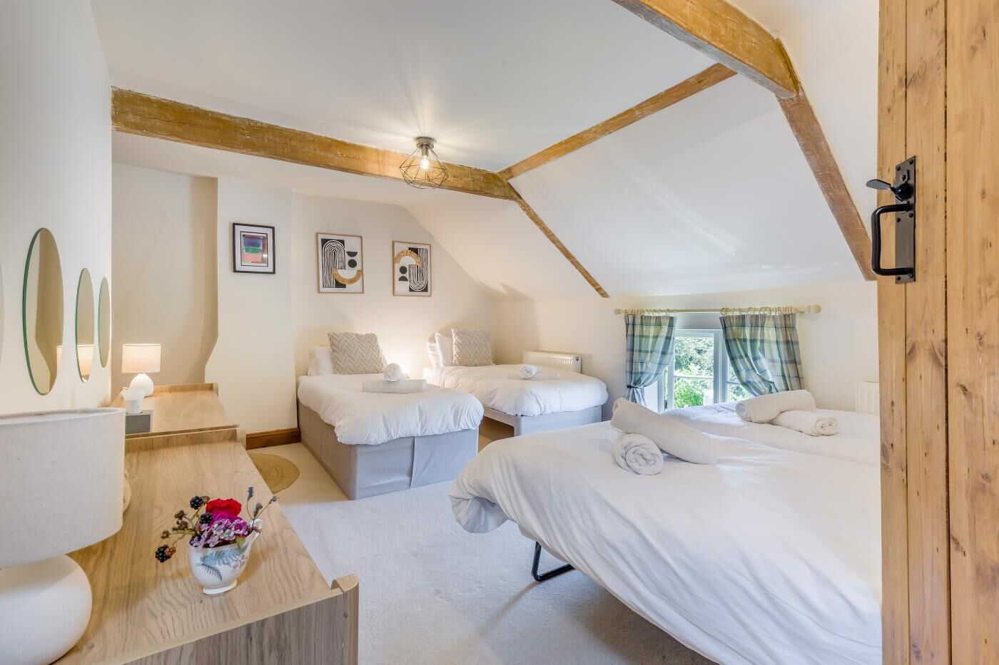 A bedroom with two beds, a wooden ceiling, and a window with curtains.