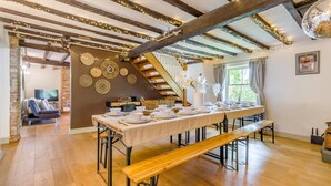 A dining area with a long table set for a meal, wooden beams on the ceiling, and a staircase leading to an upper level. - 6 Bed in Foulsham (oc-t33038) (Foulsham)