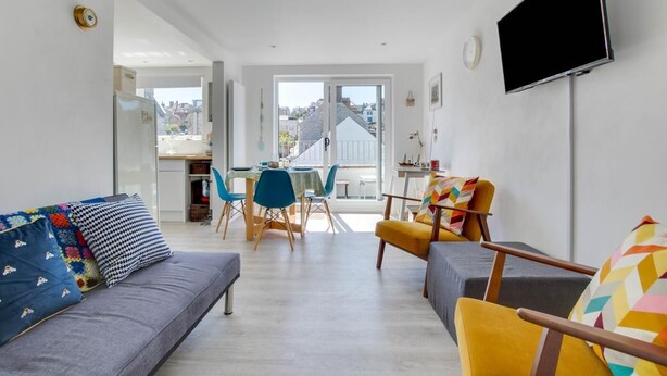 Ein modernes Wohnzimmer mit einer Couch, Sesseln und einem Essbereich mit Tisch und Stühlen.