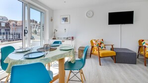 Ein modernes Wohnzimmer mit Essbereich, großen Fenstern, einem Flachbildfernseher und Blick auf die Stadt.