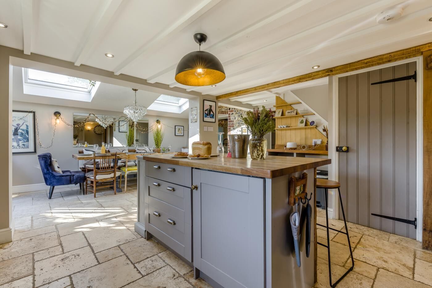 A spacious kitchen with a central island, a dining area with a blue chair, and a large window allowing natural light.