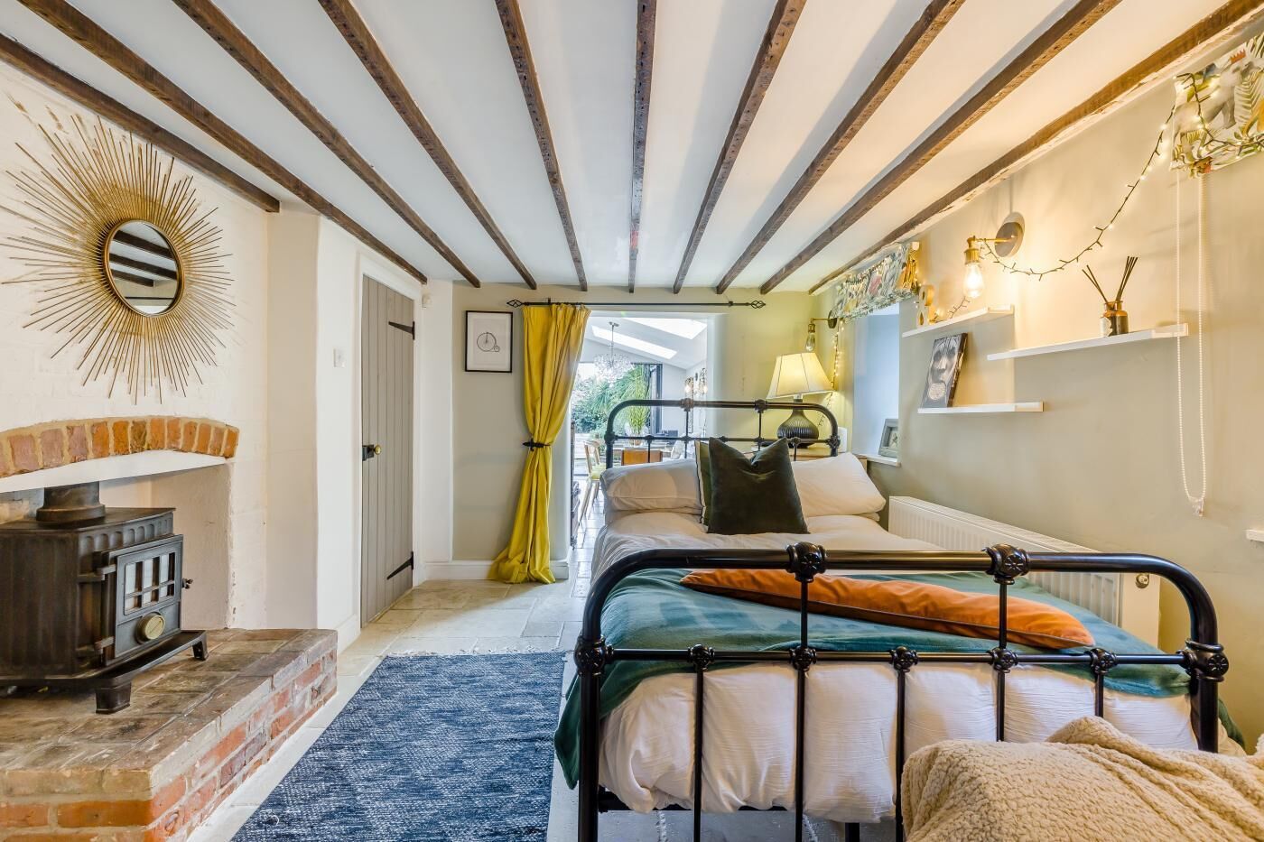 A cozy bedroom with a bed, a dresser, a mirror, and a brick fireplace.