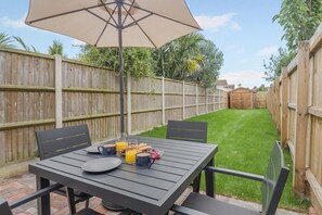 Eine Terrasse mit Tisch und Stühlen, einem großen Sonnenschirm und einem Holzzaun im Hintergrund.