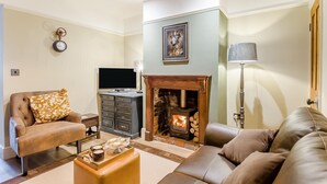 Una sala de estar con chimenea, sofás de cuero, un televisor y un reloj en la pared.