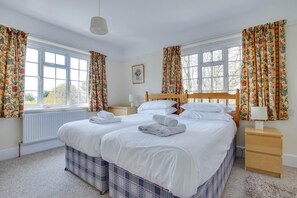 Et hotelværelse med to senge, blomstrede gardiner, et træhovedgærde, et natbord med lampe og en radiator.
