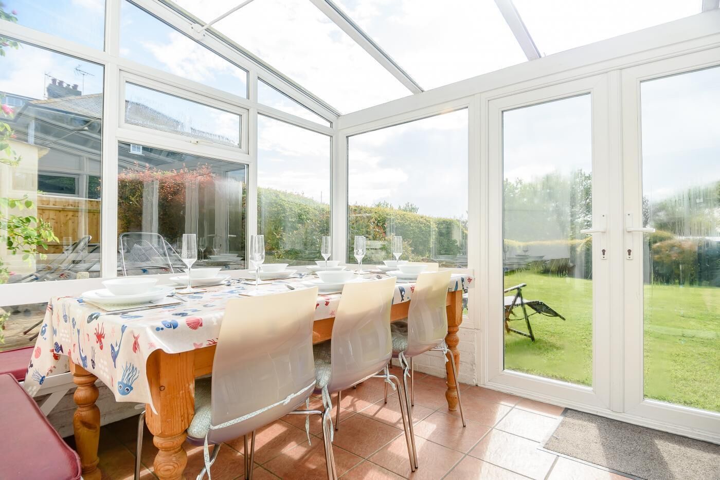 Un invernadero con una mesa de comedor para cuatro, amplias puertas de cristal y vistas a un jardín.