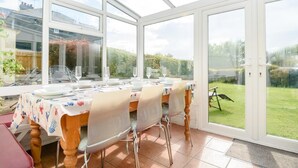 Een oranjerie met een eettafel voor vier personen, grote glazen deuren en uitzicht op een tuin.