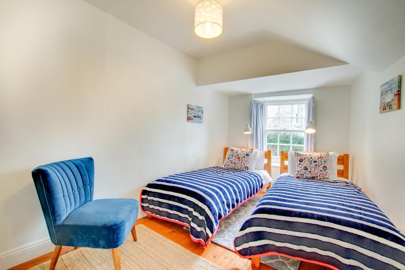 A bedroom with two beds, a blue chair, and a window with a view of greenery.
