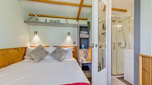 Une chambre à coucher avec un lit, une couverture rouge, une étagère avec des serviettes et un espace douche.