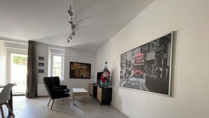 A living room with a black chair, a small table, a cabinet, and a large black and white photograph on the wall. - Villa Margot (Fumel)