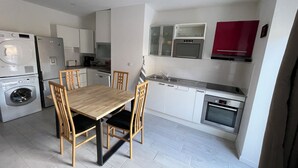 A compact kitchen with a dining table, chairs, a washing machine, a refrigerator, a microwave, and a red cabinet. - Villa Margot (Fumel)