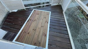 A wooden deck with a metal railing, a glass door, and a stone wall in the background. - Villa Margot (Fumel)
