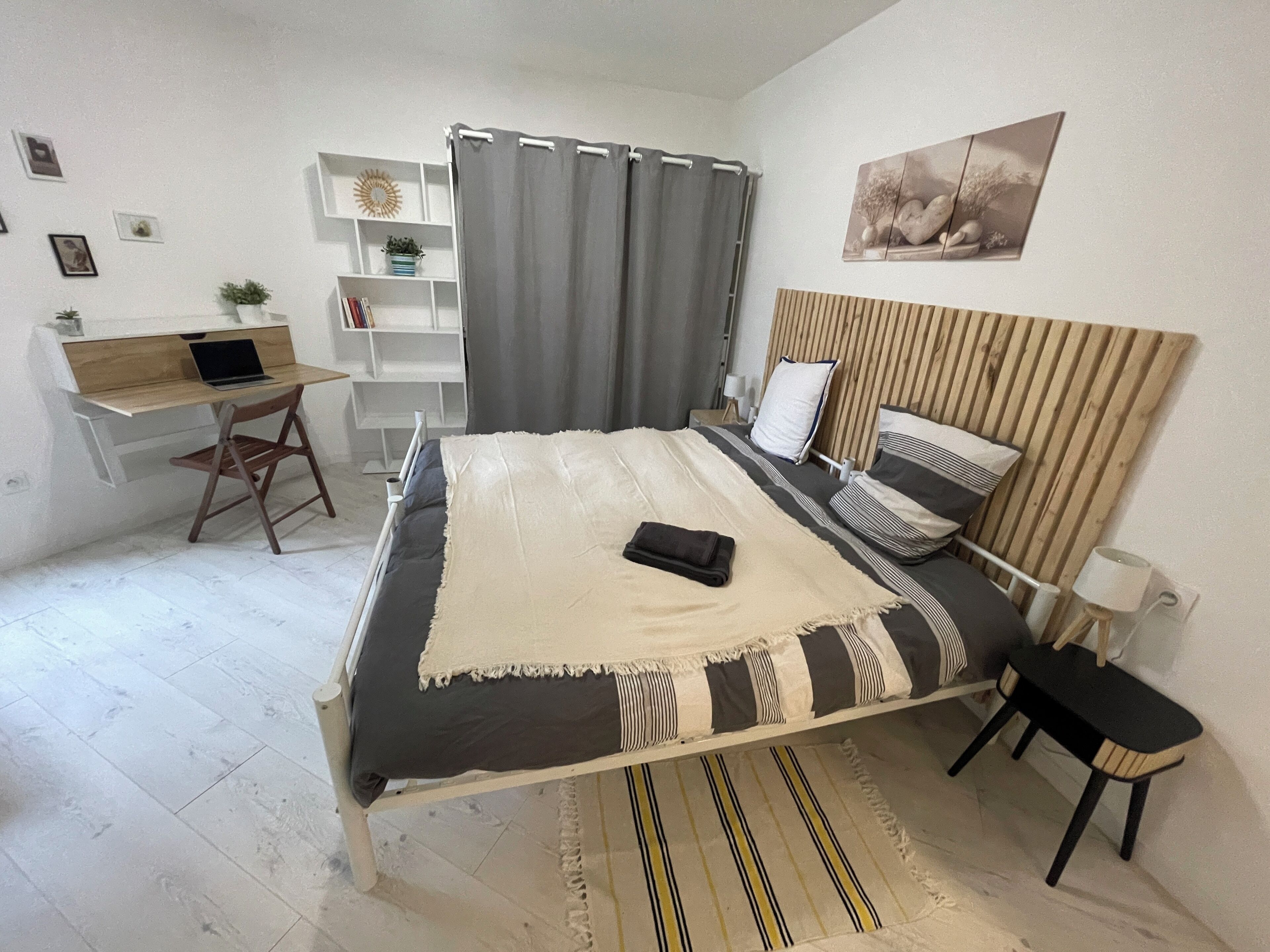 Een slaapkamer met een bed, een bureau, een stoel, een plank en een gordijn.