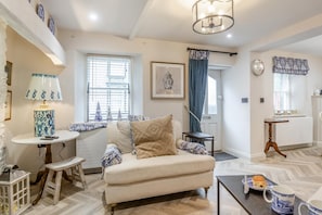 A cozy living room with a sofa, a table with a lamp, a window with blinds, and a door with a curtain. - 1 Bed in Conwy (oc-r33031) (Conwy)