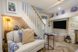 A living room with a sofa, a TV mounted on the wall, a wooden staircase, and decorative items on the walls. - 1 Bed in Conwy (oc-r33031) (Conwy)