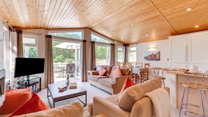 A spacious living area with a wooden ceiling, a television, a sofa, a coffee table, and a dining area with a table and chairs. - 2 Bed in Aldeburgh (oc-har) (Aldeburgh)