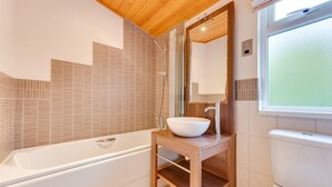 A modern bathroom with a freestanding bathtub, a wooden vanity with a large mirror, and a window providing natural light. - 2 Bed in Aldeburgh (oc-har) (Aldeburgh)