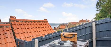 A rooftop terrace with a table set for tea, overlooking a coastal town.