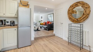 A modern kitchen with a refrigerator, microwave, and coffee maker. There is a living area with a sofa and a mirror. - 3 Bed in Sandsend (oc-a33016) (Sandsend)