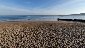 Ein sandiger Strand mit einem hölzernen Steg, der sich ins Wasser erstreckt.