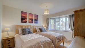 Ein Schlafzimmer mit zwei Betten, einem Nachttisch mit Lampe, einem Holztisch und einem Fenster mit Vorhängen.