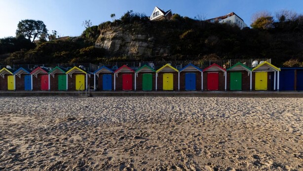 Eine Reihe bunter Strandhäuser mit einer felsigen Hügelkulisse im Hintergrund.
