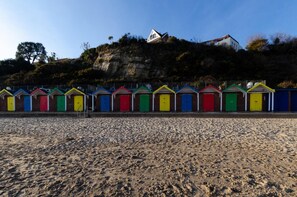A row of colorful beach huts with a rocky hillside in the background. - 2 Bed in Swanage (oc-wy421) (Swanage)