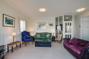 A living room with a blue armchair, green sofa, and a purple sofa. There are two lamps, a radiator, and a framed picture on the wall.