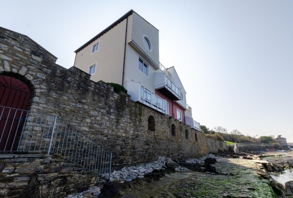 A stone wall with a metal gate, a building with a red door, and a balcony.