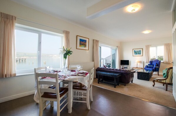 A dining area with a table set for four, a sofa, and a television in a living room.