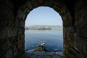 A stone archway leading to a calm body of water with a pier extending into it.