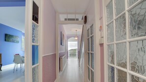 A hallway with a light-colored floor, pink walls, and a glass door with a stone pattern. There is a chair and a table in the left room. - 4 Bed in Morcombelake (oc-wy403) (Morcombelake)