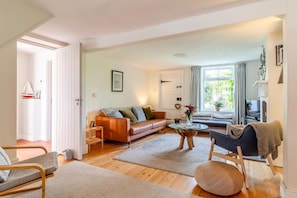 Un salon comprenant un canapé, une table basse, un fauteuil, un téléviseur et une fenêtre avec des rideaux.
