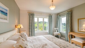 Quarto com uma cama grande, mesa de cabeceira, cadeira, escrivaninha e vista para o campo.