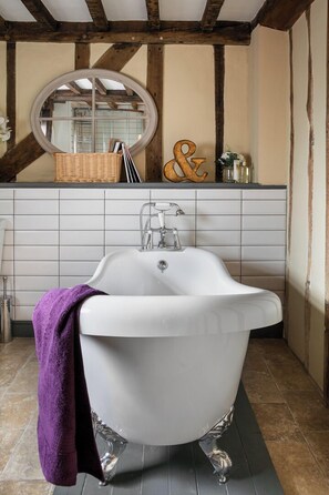 A bathroom with a white clawfoot bathtub, a round mirror, and a tiled backsplash. - 5 Bed in Halesworth (oc-cfl) (Halesworth)
