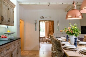 A rustic kitchen with wooden cabinets, a dining table set with plates and cutlery, and a hanging copper light fixture. - 5 Bed in Halesworth (oc-cfl) (Halesworth)