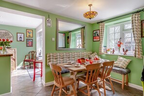A dining area with a wooden table, chairs, and a bench. There is a window with curtains and a view of the outside. - 3 Bed in Portesham (oc-wy550) (Portesham)