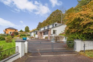 A modern two-story house with a stone facade, a large front yard, and a gated driveway. - 3 Bed in Ullapool (oc-s33063) (Ullapool)