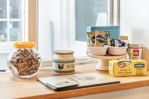 A kitchen counter with various food items, including a jar of dog treats, a sugar jar, a coffee maker, and a box of lemon & stem ginger biscuits. - 2 Bed in Swanage (oc-wy467) (Swanage)