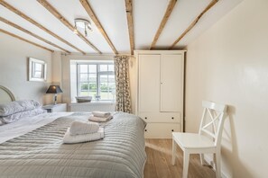 A bedroom with a bed, a chair, a nightstand, a window with curtains, and a wardrobe. - 2 Bed in Swanage (oc-wy467) (Swanage)