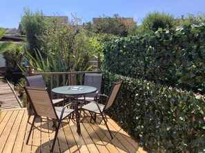 An outdoor patio with a round table and four chairs, surrounded by greenery and a hedge. - 2 Bed in Swanage (oc-wy467) (Swanage)