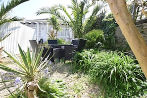 A patio area with outdoor furniture, a variety of plants, and a white building in the background. - 2 Bed in Swanage (oc-wy467) (Swanage)